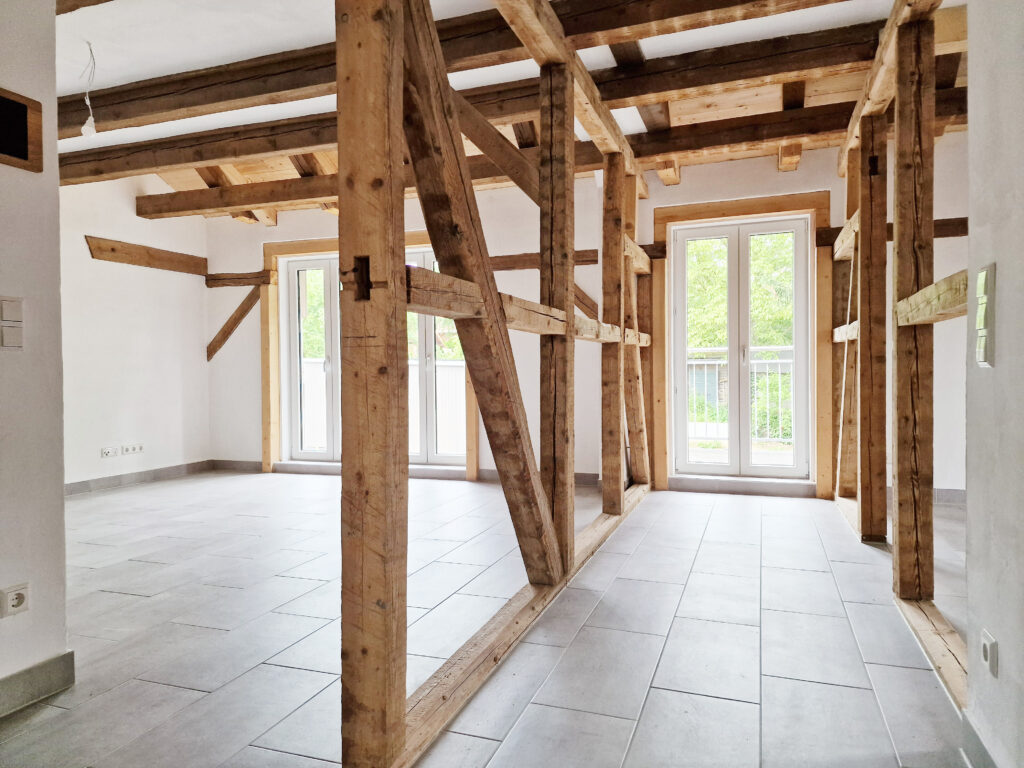 Wohnraum mit freiliegendem historischem Fachwerk, modernen bodentiefen Fenstern und hellem Fliesenboden