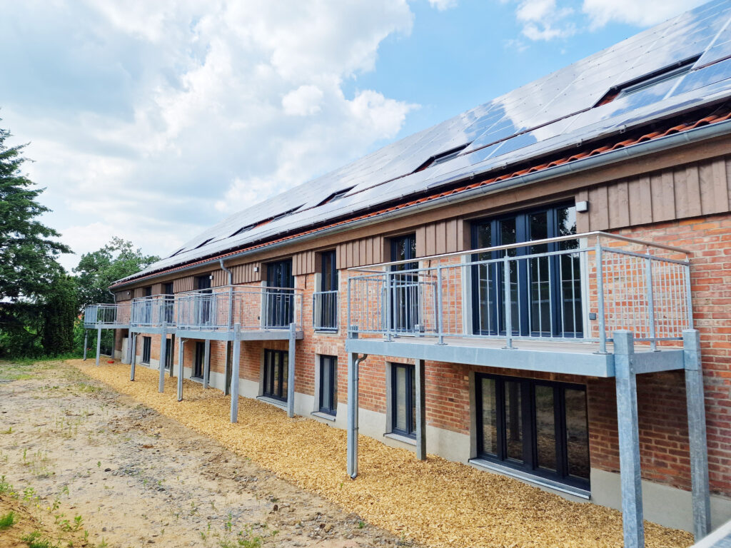 Sanierte Rückseite des Gebäudes mit Photovoltaikanlage auf dem Dach, modernen Balkonen und erhaltener Ziegelfassade