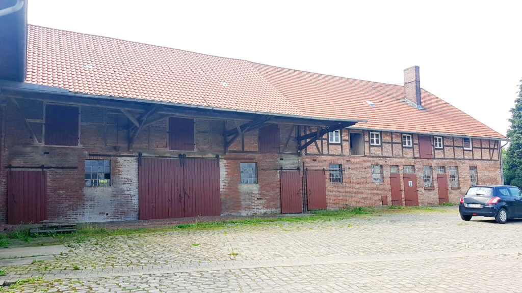 Historischer Bauernhof mit Fachwerk und Ziegelmauerwerk, Hofseite mit großen Holztoren und Kopfsteinpflaster vor der Sanierung