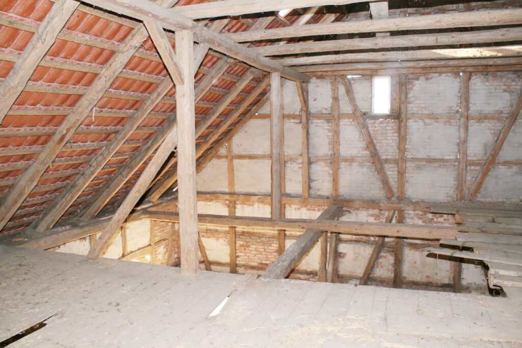 Dachstuhl der historischen Scheune mit sichtbarem Fachwerk, Ziegelausfachung und Dachziegeln von innen vor der Sanierung
